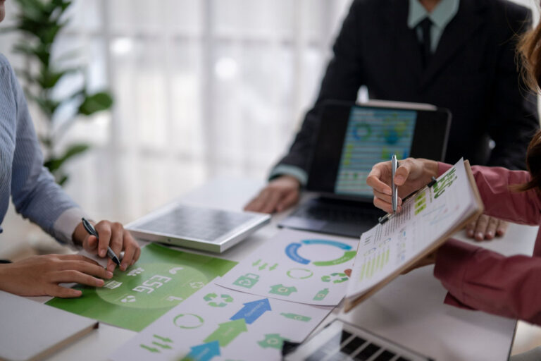 A business meeting scene with hands pointing at ESG (Environmental, Social, Governance) documents and charts on a white desk, emphasizing sustainability and corporate responsibility.