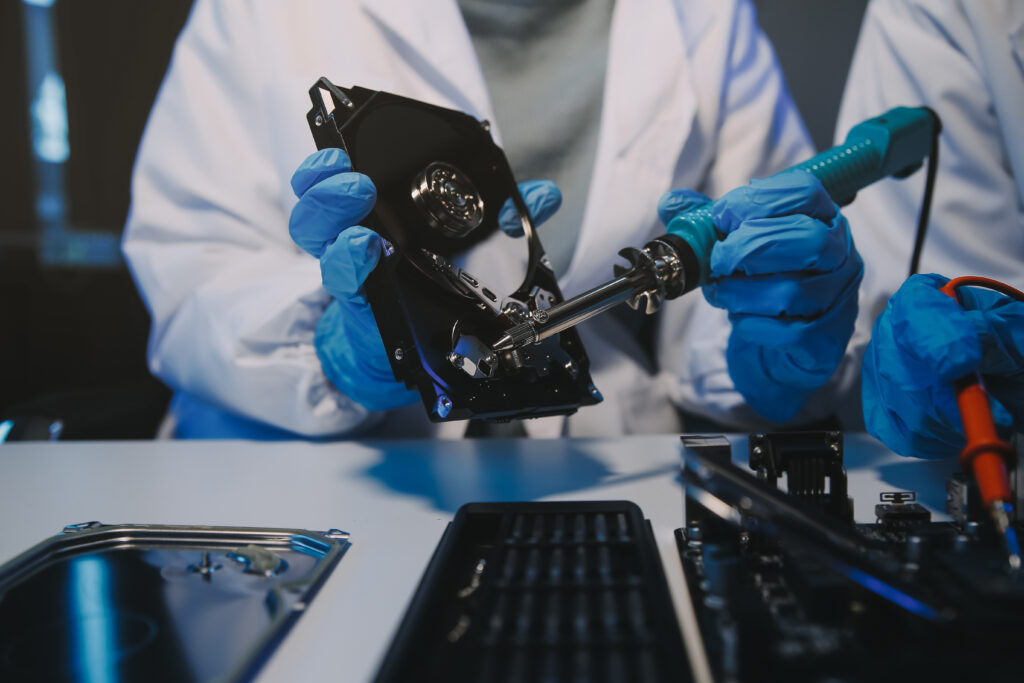 Technicians handling an opened hard drive and internal components, illustrating preparation of a data storage device for secure data destruction and compliant end-of-life processing.