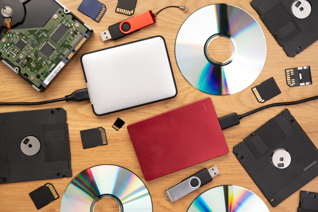 Collection of hard drives, floppy disks, optical discs, USB drives, and memory cards illustrating the many storage media types that may require secure media destruction.