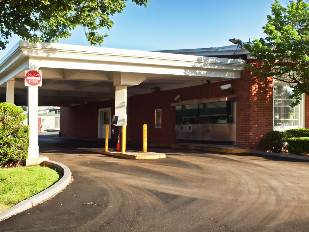 Exterior of a bank drive-thru with a white canopy, yellow bollards, and a do not enter sign on a sunny day.
