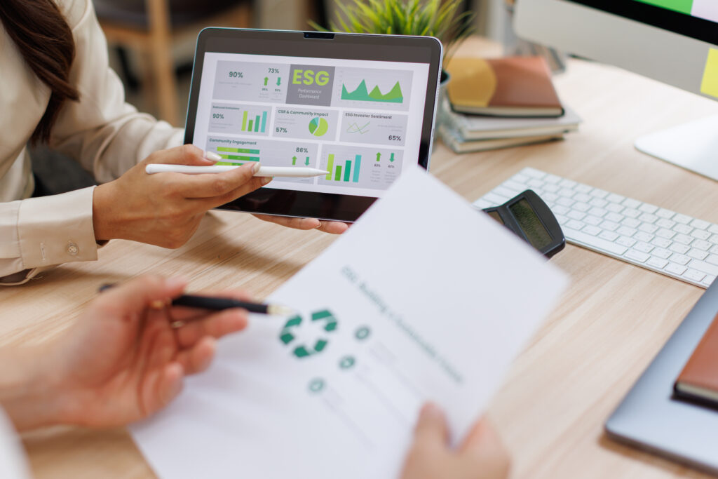 Two professionals review an ESG performance dashboard on a tablet alongside a printed recycling report at an office desk.
