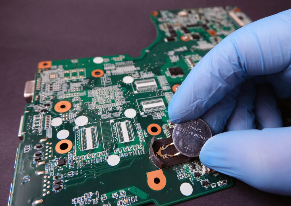 Gloved hand removing a battery from a motherboard for circuit board recycling