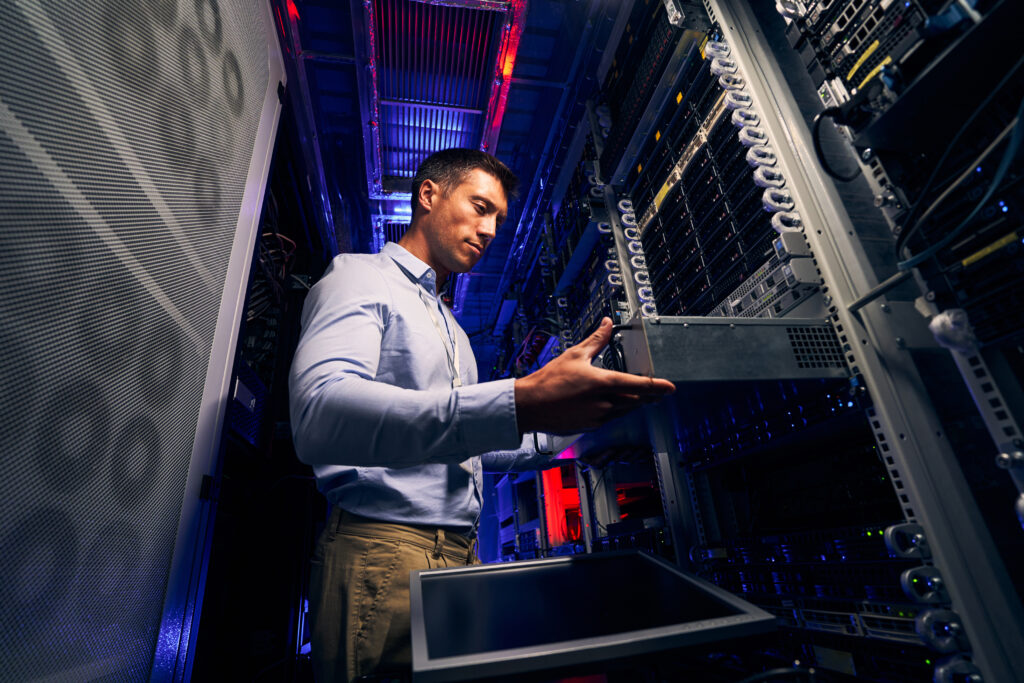 IT technician installing a rackmount server in a modern data center with illuminated server racks.