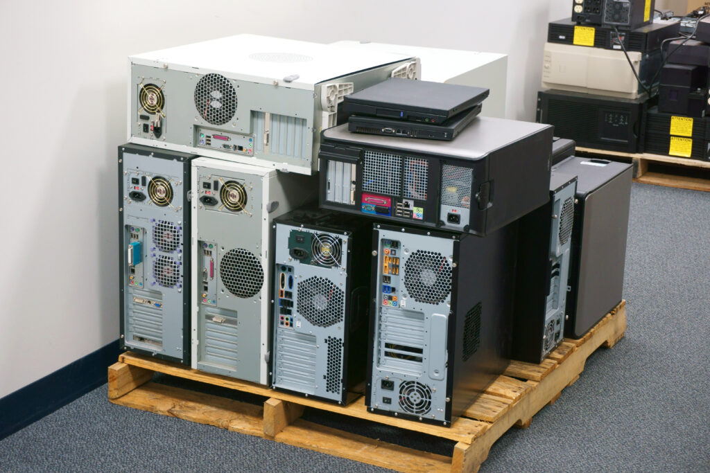 Decommissioned desktop computers and laptops stacked on pallets.