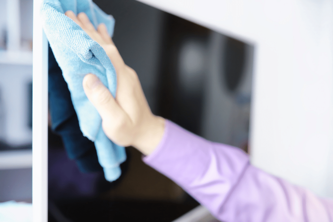 A person cleaning a computer monitor with a microfiber cloth.