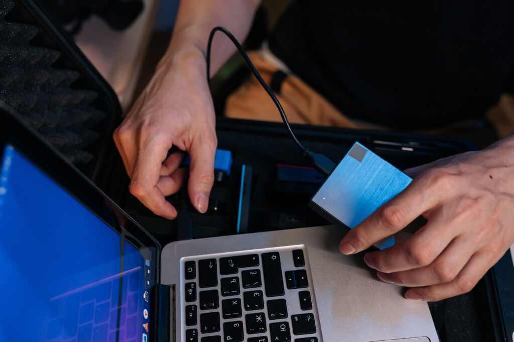 Person holding an external hard drive beside a laptop.