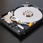 A disassembled open hard disk drive HDD of a computer or laptop lies on a dark matte surface.