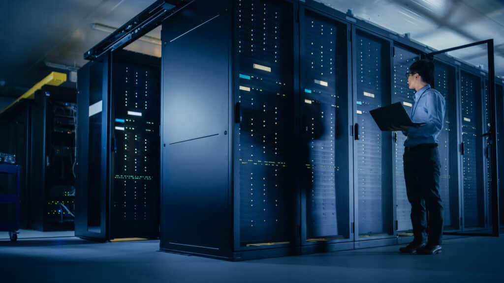 IT engineer holding a laptop while monitoring server racks in a modern data center.
