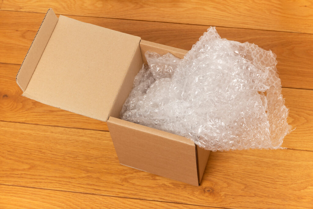 An open cardboard box filled with protective bubble wrap on a wooden floor.