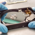 Technician wearing blue gloves removing a hard drive from its casing, illustrating secure media handling and the importance of data protection standards.