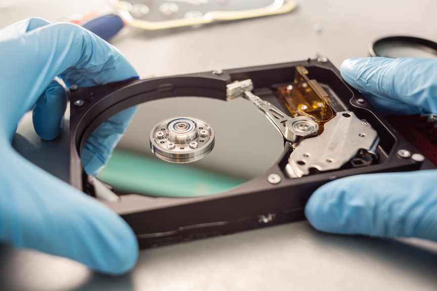 Technician wearing blue gloves removing a hard drive from its casing, illustrating secure media handling and the importance of data protection standards.