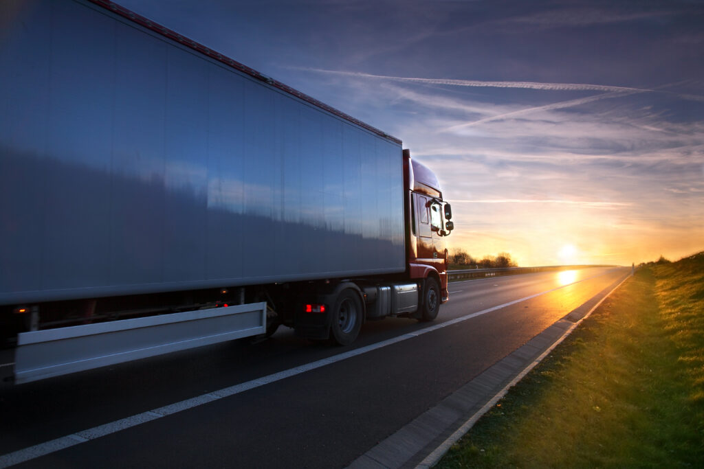 Semi-truck driving on a highway at sunset with a colorful sky and motion blur, representing freight transportation and logistics.