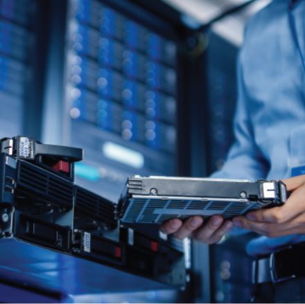 IT technician removing a server hard drive from a rack in a data center for secure disposal, representing hardware decommissioning and data destruction standards.