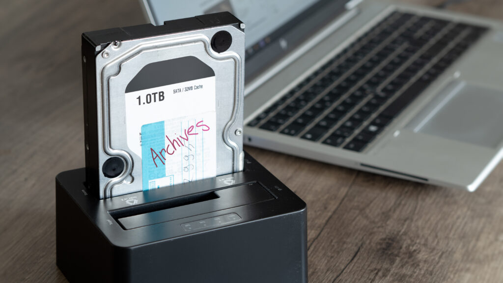 Hard drive in a docking station beside a laptop, representing certified data destruction services and secure data management.