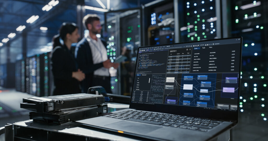 Laptop displaying storage and system management software beside hard drives in a data center, illustrating enterprise storage management and infrastructure oversight.