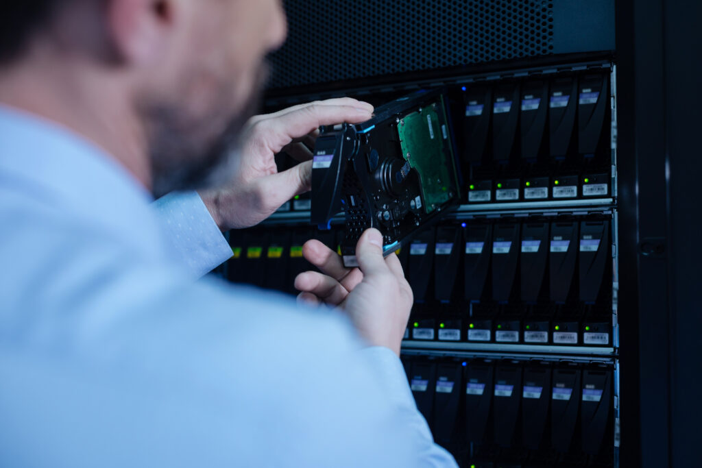 IT technician removing or installing a SAS hard drive in a server rack, representing enterprise storage management and data center maintenance.