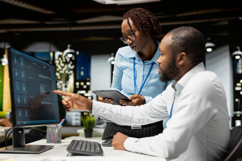 Two professionals reviewing information on a computer in an office, representing IT asset tracking, lifecycle planning, and operational decision-making.