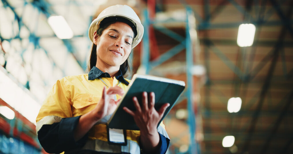 Warehouse professional using a tablet in a distribution facility, representing IT asset tracking, logistics, and lifecycle management.