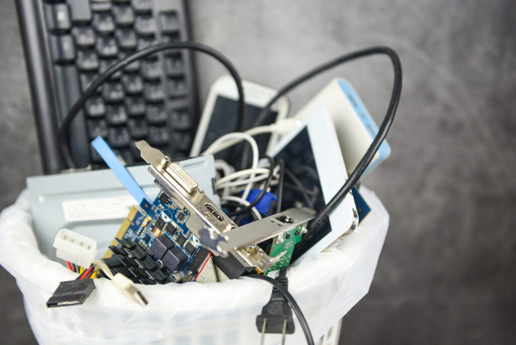 Example of what constitutes e-waste: an office bin filled with discarded electronics, including a keyboard, cables, circuit boards, and mobile devices.