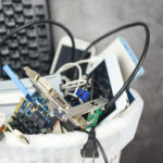 Example of what constitutes e-waste: an office bin filled with discarded electronics, including a keyboard, cables, circuit boards, and mobile devices.