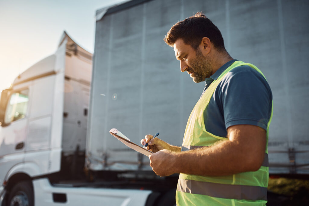 A logistics team member holds a clipboard while standing next to a truck.