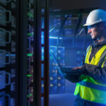 IT technician in safety gear working on a laptop in a modern data center