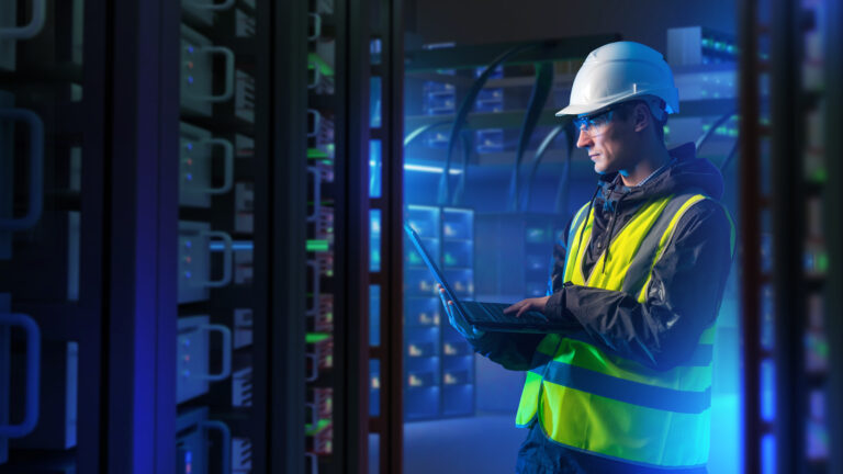 IT technician in safety gear working on a laptop in a modern data center