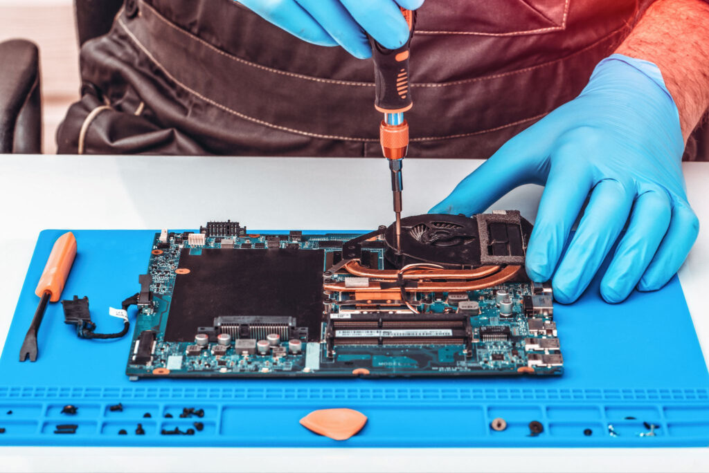 Technician repairing a laptop motherboard on a blue magnetic mat